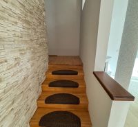 Eine enge Treppe mit braunen Stufen und einer Wand mit Steindekor in einem Einfamilienhaus.