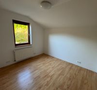 Ein Zimmer in einem Einfamilienhaus mit einem Boden in Holzoptik und einem Heizkörper unter dem Fenster.