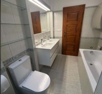 Ein Badezimmer mit Badewanne und Toilette in einem Einfamilienhaus, weiße Fliesen und Holztüren.