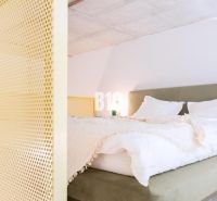 Schlafzimmer in einer 2-Zimmer-Wohnung mit Bett und gelber Trennwand.