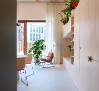 Helle Innenausstattung einer 2-Zimmer-Wohnung mit Pflanzen, einem bequemen Sessel und Regalen.