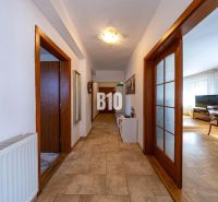 Ein Flur mit Fliesenboden, der zu einem Wohnzimmer in einem Einfamilienhaus führt, Holztüren.