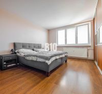 Schlafzimmer mit großem Bett, Nachttisch und Boden mit Holzdekor in einer 3-Zimmer-Wohnung.