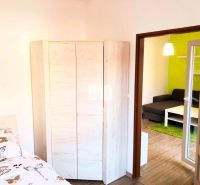 Schlafzimmer mit Eckschrank, nebenan der Eingang zum Wohnzimmer mit Sofa.