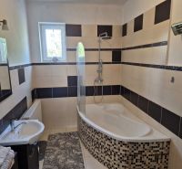 Badezimmer im Einfamilienhaus mit Badewanne, Fliesen und Fenster; dezente Ausstattung und Leuchte.