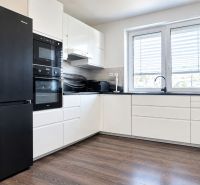 Küchenzeile mit schwarzen Geräten und einem Boden in Holzoptik in einem Einfamilienhaus.