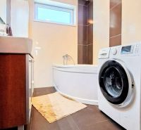 Badezimmer im Einfamilienhaus mit Badewanne, Waschmaschine und dunklen Fliesen im dekorativen Design.