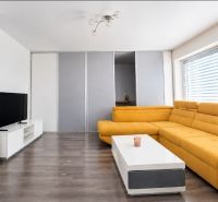 Wohnzimmer in einem Einfamilienhaus mit gelbem Sofa, Fernseher und Holzboden.