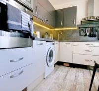 Küche mit weißen und grauen Schränken in einer 2-Zimmer-Wohnung, Boden mit Holzdekor.