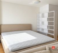 Schlafzimmer in einer Einzimmerwohnung mit Bett und weißen Regalen, Holzboden.