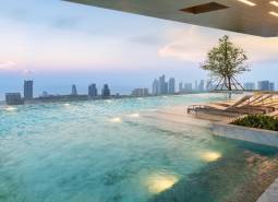 Ein Pool mit Liegestühlen und Blick auf die Skyline von Pattaya, Wohnungsbau.