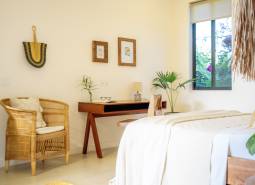 Helles Schlafzimmer in einem Einfamilienhaus mit einem Rattansessel und einem Holztisch.