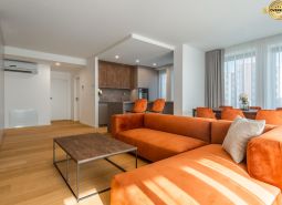 Wohnzimmer mit orangefarbenem Sofa, Küche und Holzboden im Wohnungsbauprojekt.