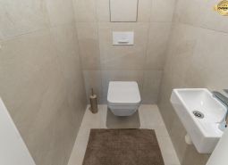 Hänge-WC, kleines Waschbecken und beigefarbene Fliesen im Badezimmer, Wohnungsbau.