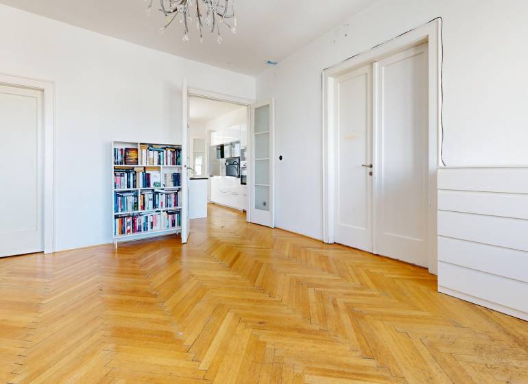 Ein geräumiges Zimmer in einer 3-Zimmer-Wohnung mit Bibliothek, Parkettboden und weißen Türen.