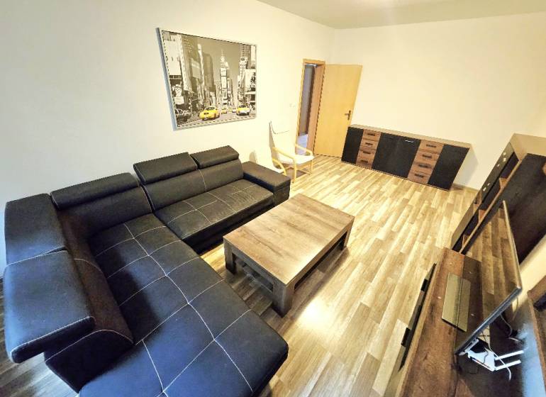 Wohnzimmer in einer 3-Zimmer-Wohnung mit schwarzem Sofa und Holzmöbeln.