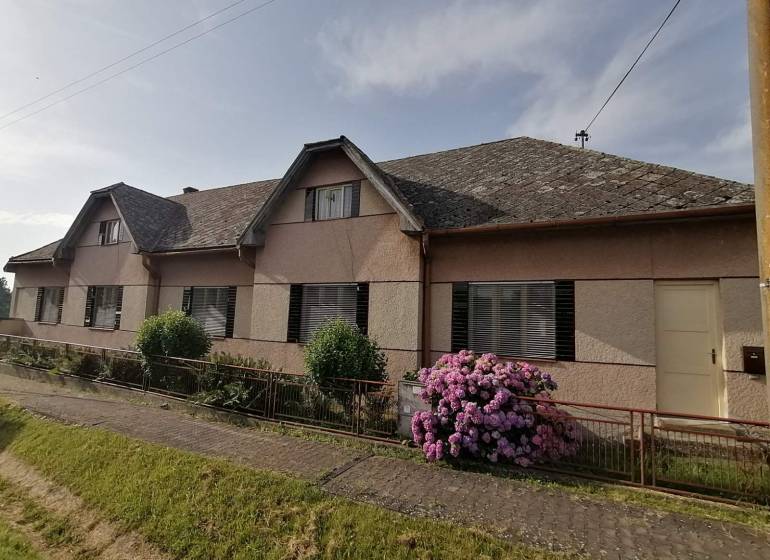 Ein Einfamilienhaus in Hrkovce mit Blumen vor dem Zaun und einem Schrägdach.