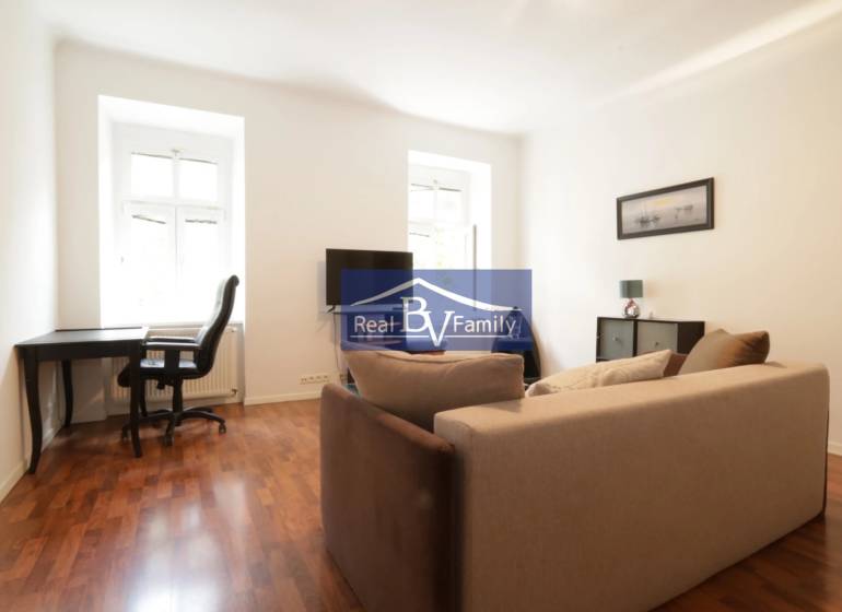 Wohnzimmer in einer Zweizimmerwohnung mit Sofa, Schreibtisch und Fernseher.