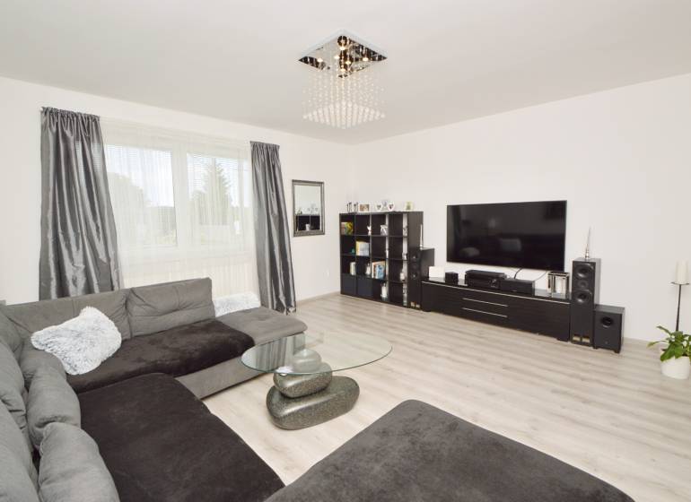 Wohnzimmer mit großer Couch, Glastisch und Fernseher in einem Einfamilienhaus.