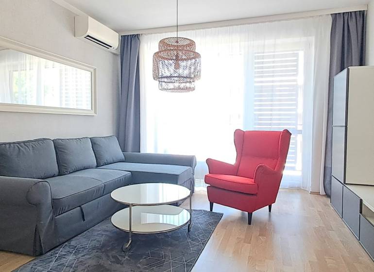 Wohnzimmer mit einem bequemen Sofa, einem roten Sessel und einem Fernseher in einer 2-Zimmer-Wohnung.