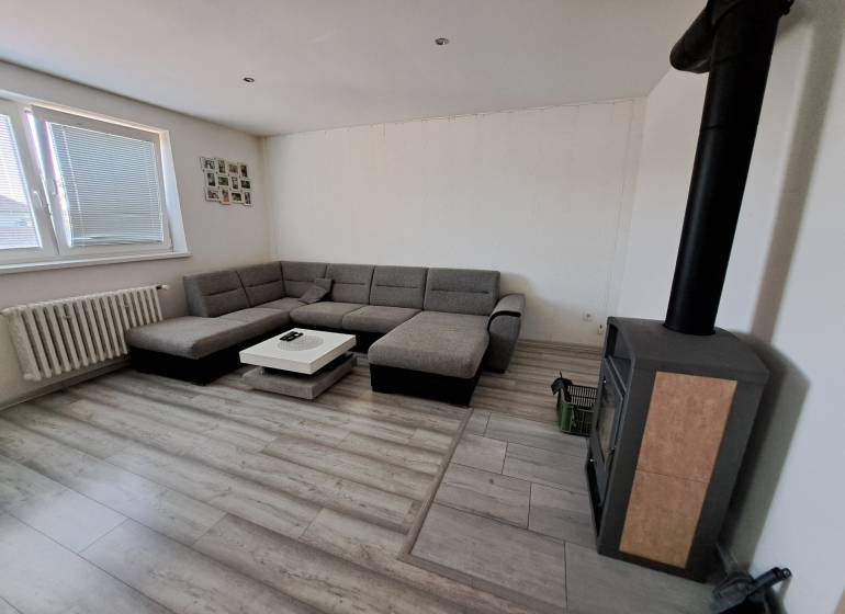 Wohnzimmer mit Ecksofa, Kaminofen und Tisch in einem Einfamilienhaus.