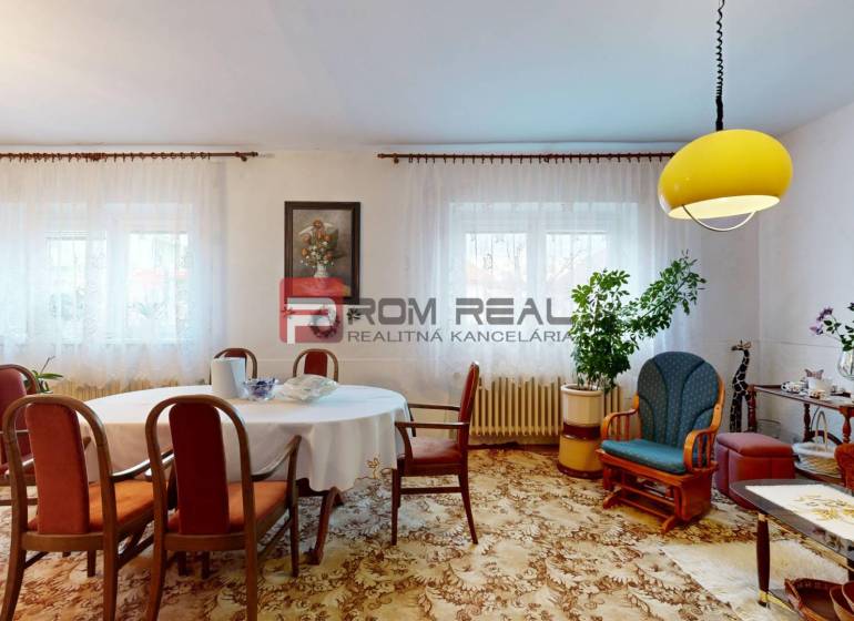 Wohnzimmer in einem Einfamilienhaus mit Tisch, Stühlen, Dekorationen und einer gelben Deckenleuchte.