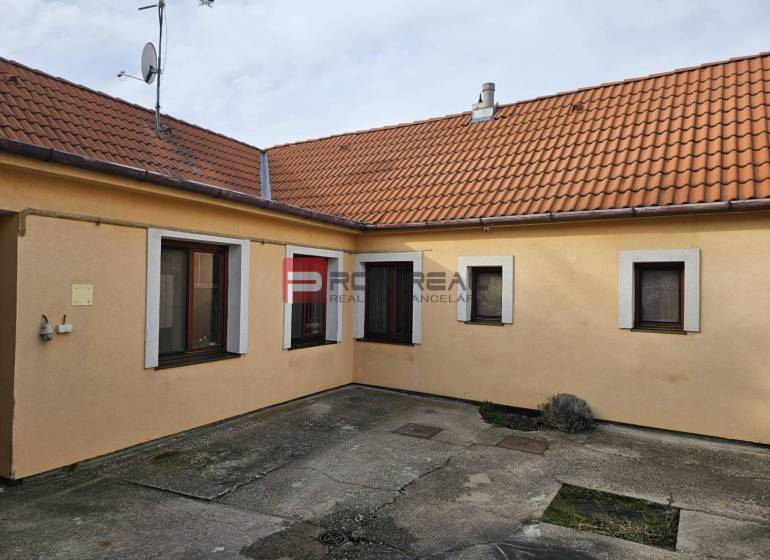 Der Hof des Einfamilienhauses in der Sonnenstraße in Pezinok mit Betonpflaster und orangefarbener Fassade.