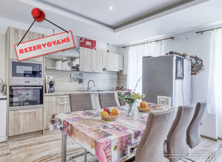 Küche in einer 2-Zimmer-Wohnung mit Tisch, Geräten und dem Schild 