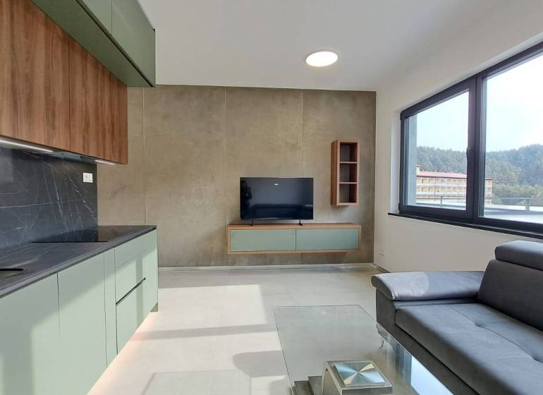 Küchenzeile mit Fernseher und Sofa in einer 2-Zimmer-Wohnung mit großem Fenster.
