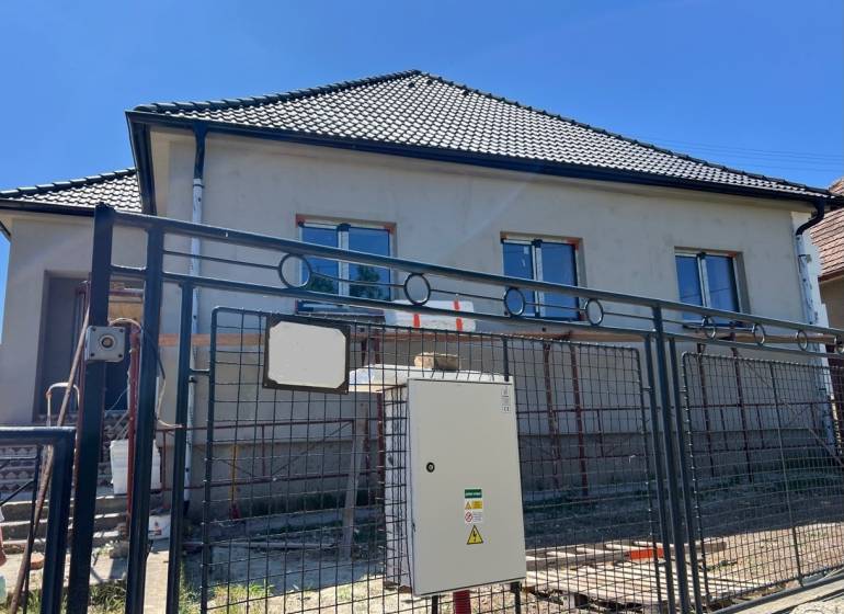 Ein Einfamilienhaus in Sasinkovo in der Sasinkovo-Straße mit unvollendeter Fassade hinter einem Metallzaun.