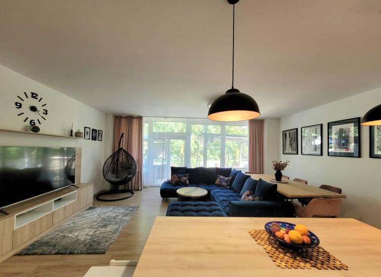 Wohnzimmer in einer 3-Zimmer-Wohnung mit einem blauen Sofa, großen Fenstern und einem Hängesessel.