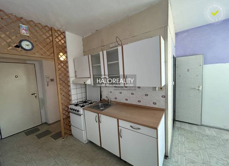 Küche in einer Einzimmerwohnung mit Gasherd und Schränken an der weißen Wand.