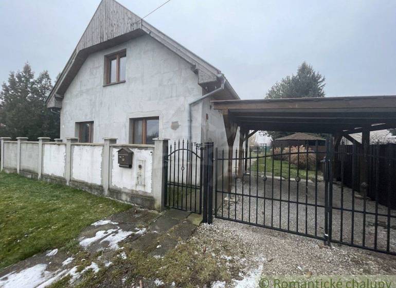 Ein Einfamilienhaus mit weißer Fassade und Tor, umgeben von Rasen und Zaun.