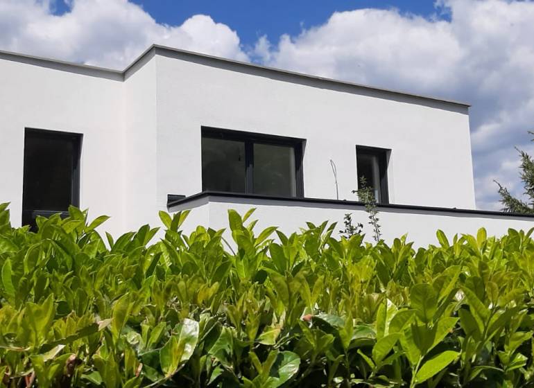 Villa in Hainburg an der Donau mit weißer Fassade, umgeben von Grün unter blauem Himmel.