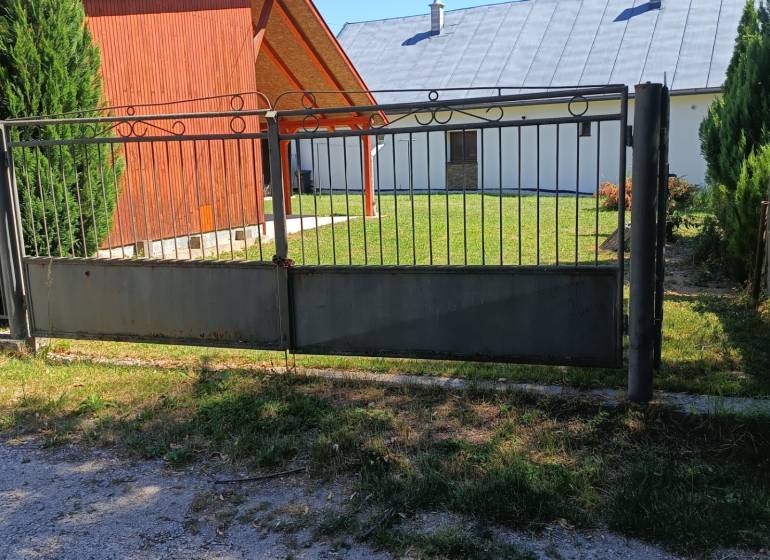 Ein Tor und eine Holzhütte in Tužina, umgeben von Rasen und Nadelbäumen.
