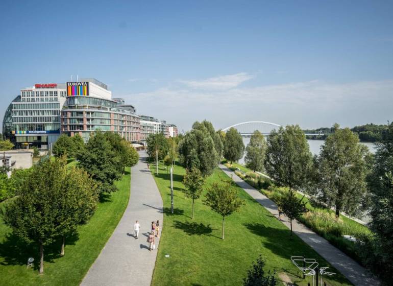 Eurovea in Bratislava, Neue Stadt, Flussufer mit Gehweg und grünen Bäumen.