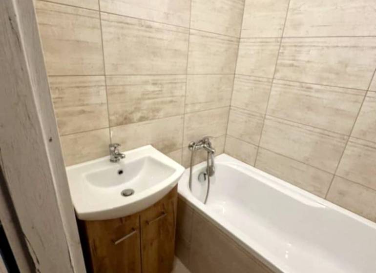 Badezimmer in einer 2-Zimmer-Wohnung mit Badewanne und Waschbecken in Holzdekor.