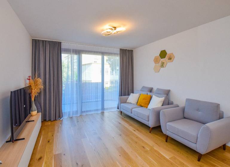 Wohnzimmer mit bequemer Couch, Holzboden und Fernseher in einer 3-Zimmer-Wohnung.