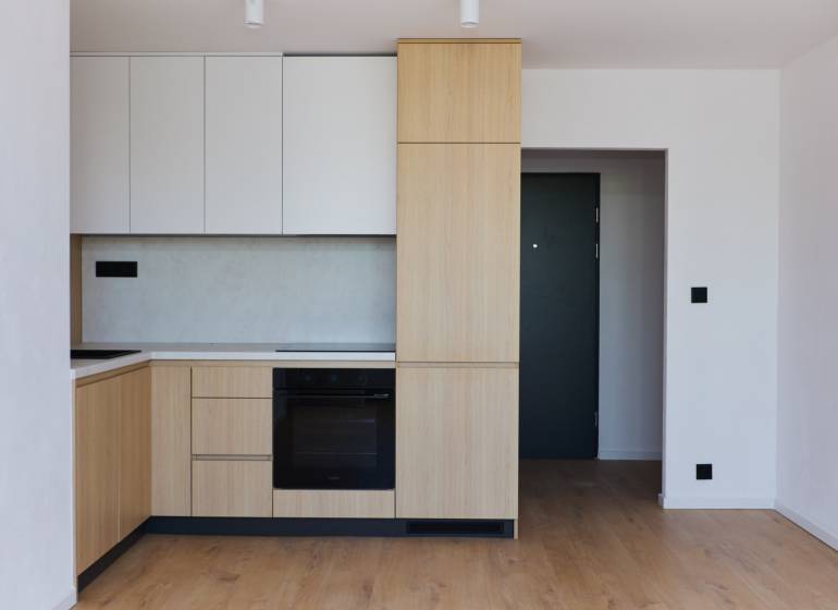 Küche in einer 2-Zimmer-Wohnung mit Holzschränken und schwarzen Geräten.