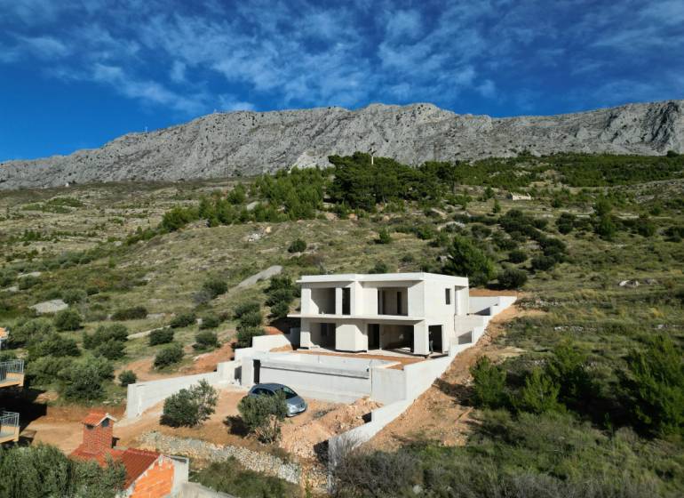 Eine Villa in Duće, umgeben von Grün und Bergen, mit blauem Himmel im Hintergrund.