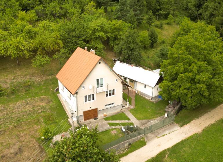 Ein Einfamilienhaus in Papradno, umgeben von einem grasbewachsenen Grundstück und Bäumen, mit einer Zufahrtsstraße.