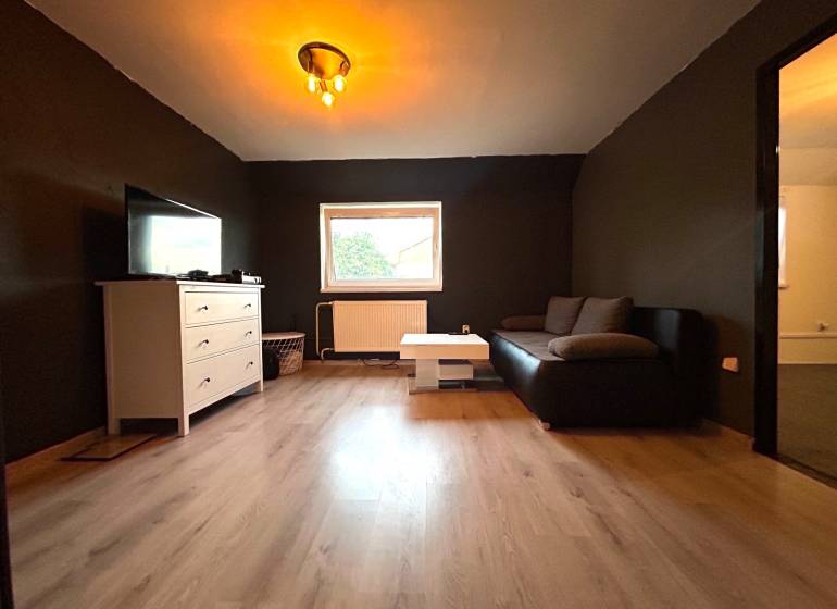 Wohnzimmer in einer Vierzimmerwohnung mit schwarzem Sofa und weißer Kommode.