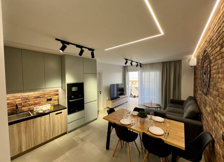 Wohnzimmer mit Küche im Ferienapartment. Ziegelwand, Esstisch und bequeme Couch.