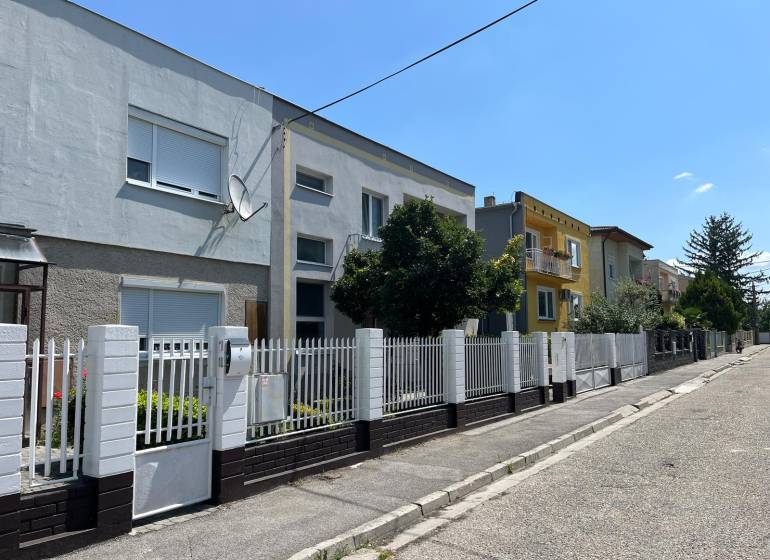 Eine Straße mit Einfamilienhäusern in Komárno, mit einem weißen Zaun und einer Satellitenschüssel.