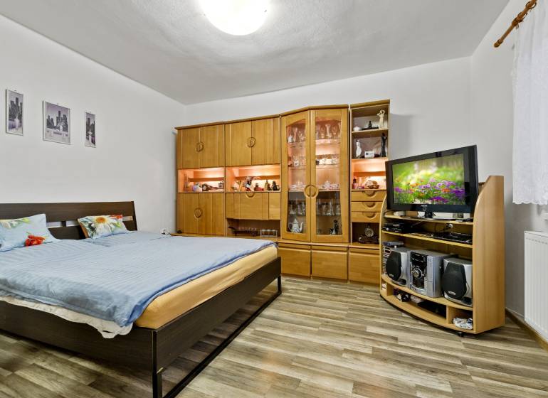 Schlafzimmer mit Doppelbett, Wohnwand aus Holz und Fernseher in einer Zweizimmerwohnung.