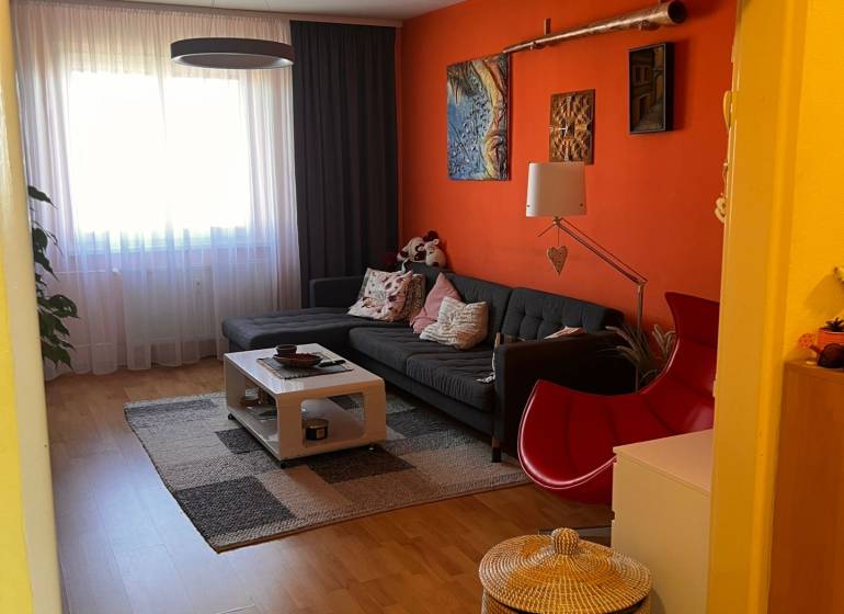 Wohnzimmer einer 3-Zimmer-Wohnung mit orangefarbener Wand, Sofa und Couchtisch.
