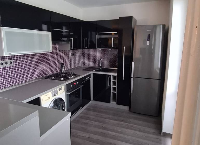 Küche in einer 2-Zimmer-Wohnung mit Geräten, dunklen Möbeln und lila Fliesen.