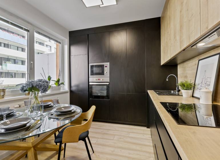 Küche in einer 2-Zimmer-Wohnung mit Esstisch und moderner schwarzer Küchenzeile.