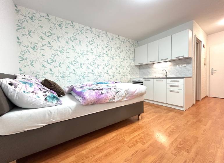 Einzimmerwohnung mit Bett, Küchenzeile und Blumenmuster an der Wand.