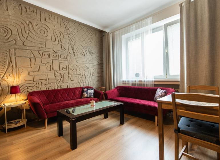 Wohnzimmer in einer Zweizimmerwohnung mit gemusterter Wand und roten Sofas.